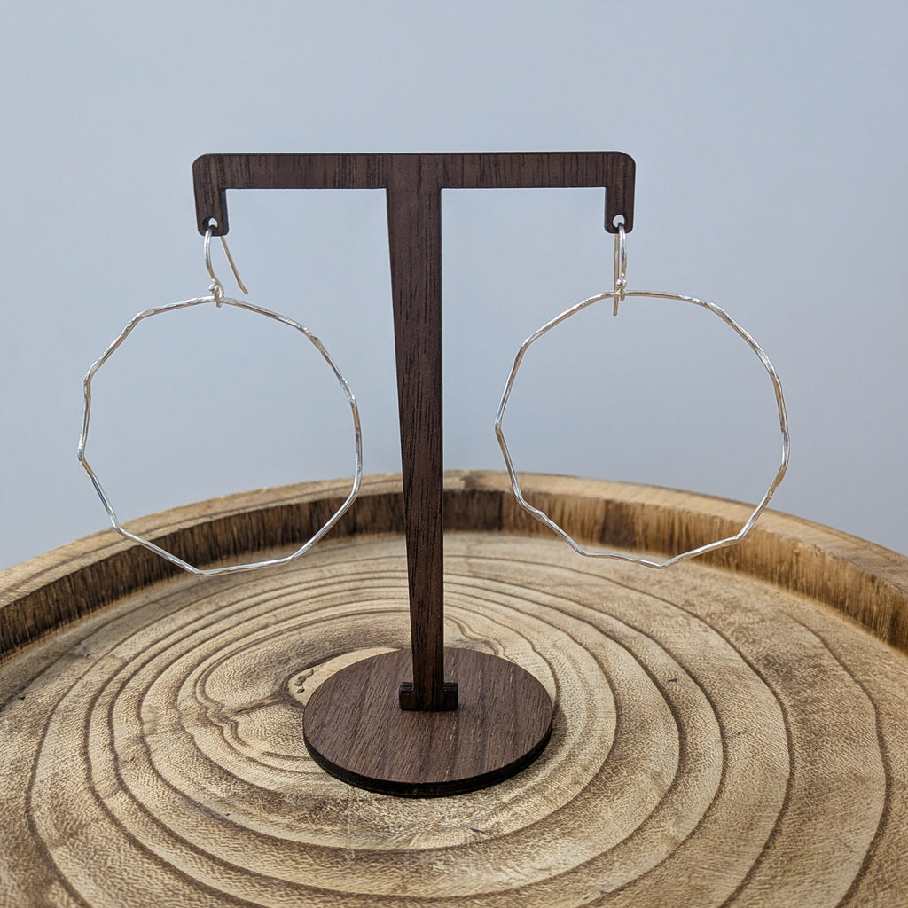 Wooden earring stand with two hoop earrings on a wooden surface.